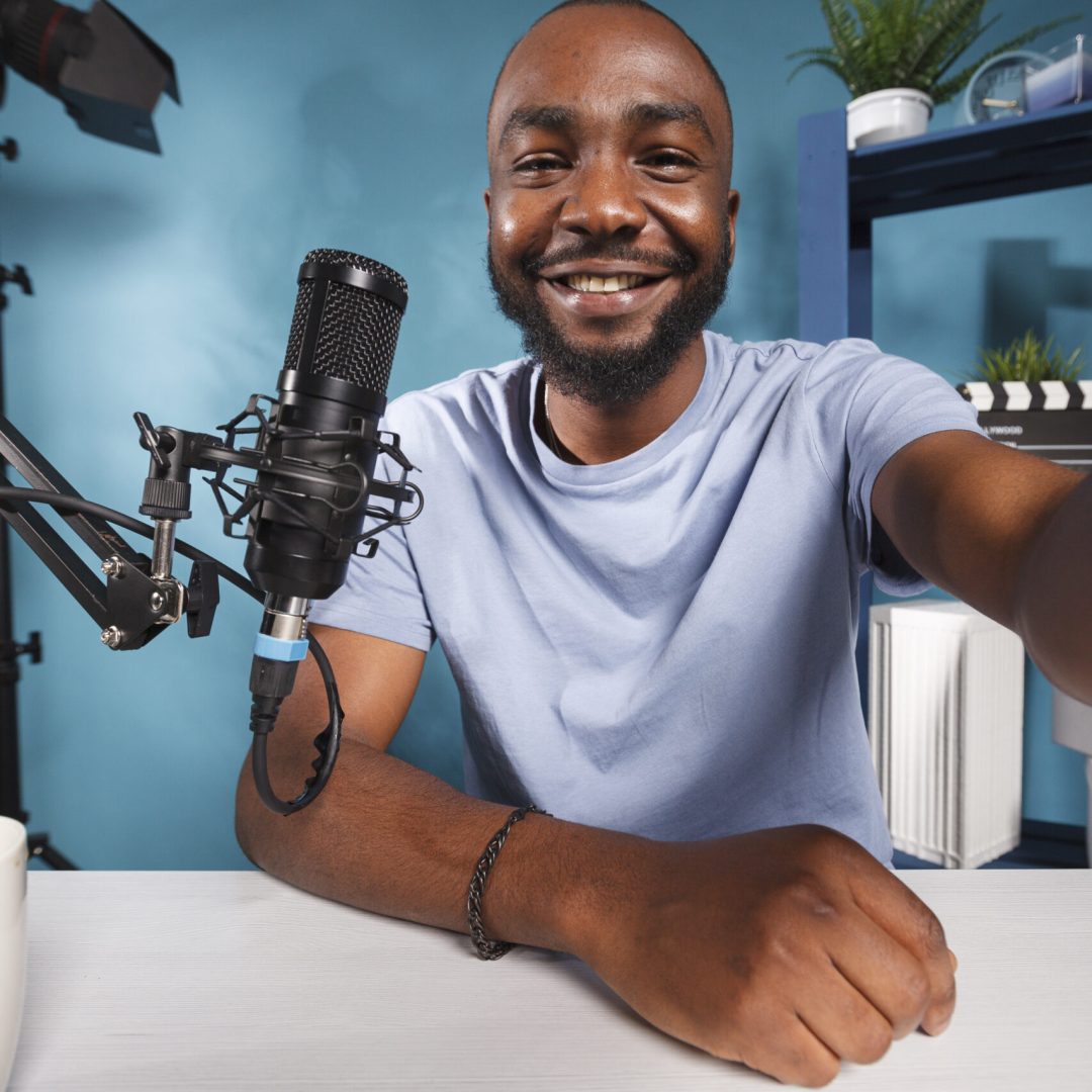 Smiling african american blogger speaking in microphone and holding camera portrait. Cheerful streamer talking with subscribers while recording video for internet channel