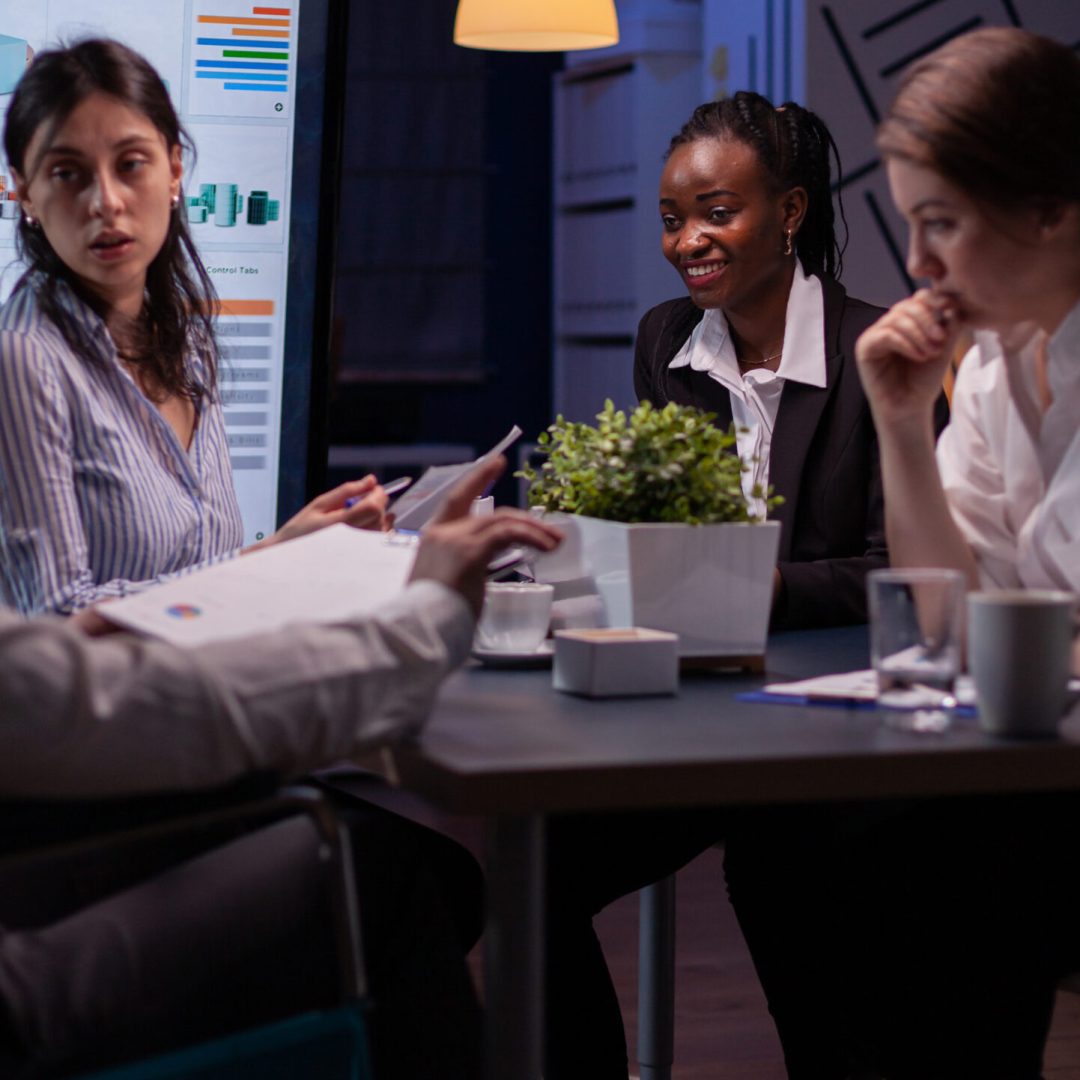 Overworked handicapped businessman in wheelchair sharing financial paperwork statistics overworking in business office meeting room. Diverse multi-ethnic brainstorming company ideas in evening